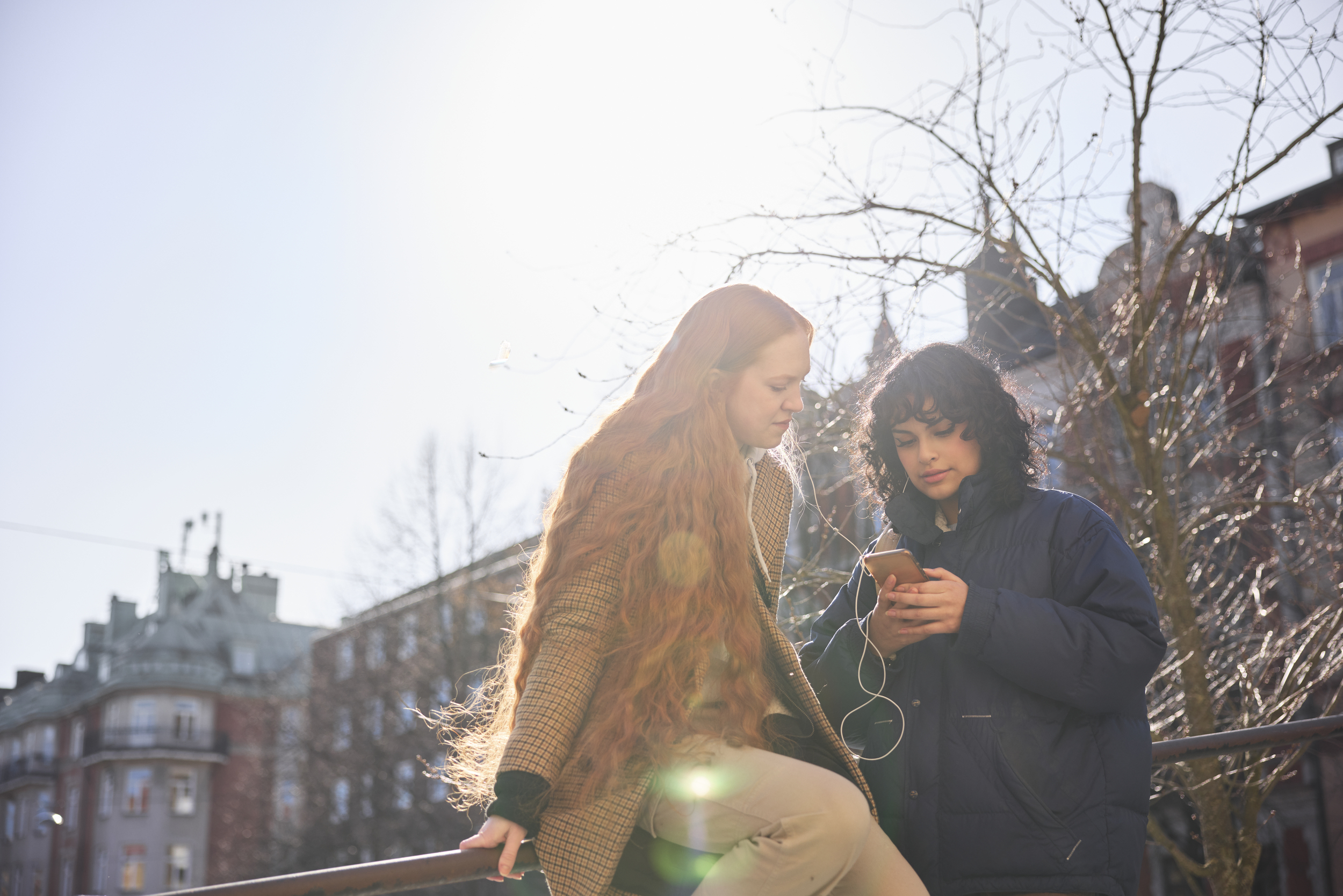 Two women looking down at a mobile phone in the city